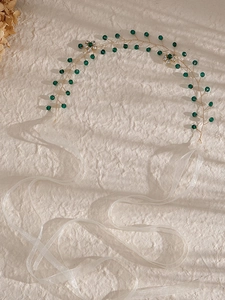 Dettaglio di perline verdi e fiori di cristallo su fascia da sposa dorata con nastri