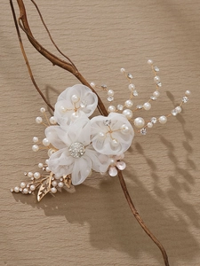 Detail of bridal hair clip with organza flowers, pearls, and gold leaf on branch