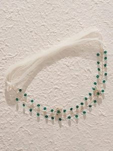 Dettaglio di un accessorio per capelli da sposa con cristalli verde smeraldo e filo d'oro