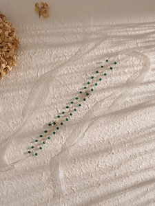 Dettaglio di perle verdi e fiori di strass scintillanti su una fascia da sposa dorata