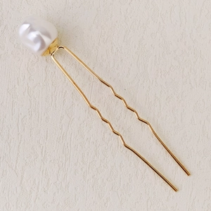 Vue détaillée d'une épingle à cheveux en U dorée avec une perle baroque et un design ondulé