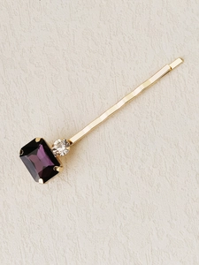 Close-up of golden bobby pin with large rectangular purple gemstone and clear crystal