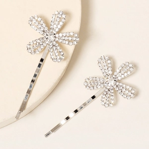 Close-up of two silver flower hair clips with sparkling rhinestones on a white stand