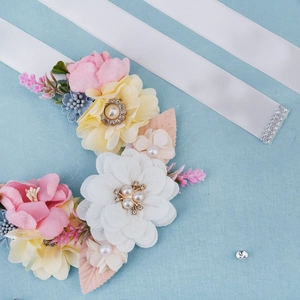 Detail of bridal sash featuring handmade pink flowers with pearls and rhinestones on satin ribbon