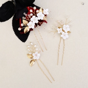 Close-up of handmade bridal hair pins with golden leaves and white resin flowers