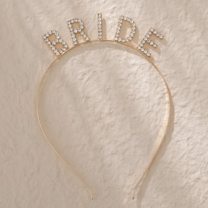 Detailed view of a gold bride headband with white rhinestones on a beige background