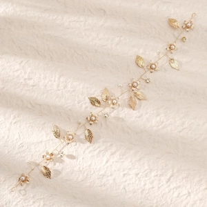 Elegant gold bridal hair vine with pearls and hollow leaves on a textured beige surface