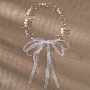 Detailopname van witte bloemen en parels op de gouden bruidshaarband met organza lint