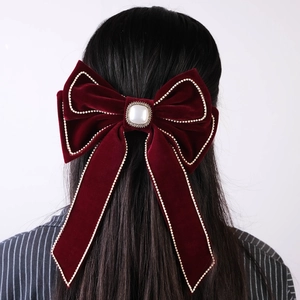 Macro detail of wine red velvet bow hair clip with faux pearl and rhinestone trim