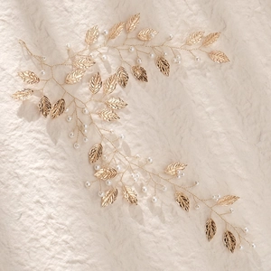 Detail eines handgefertigten Goldblatt-Haarranken mit Perlen auf beigem Stoff