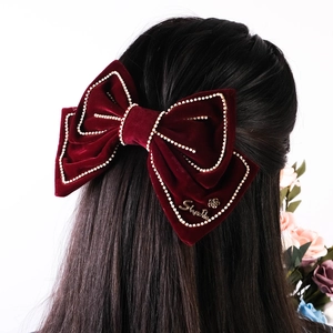 Detailed view of red velvet bow hair clip with pearl trim on long black hair