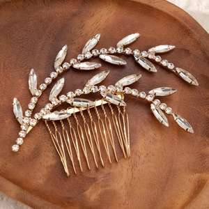 Close-up of golden leaf bridal hair comb with marquise rhinestones on wooden tray