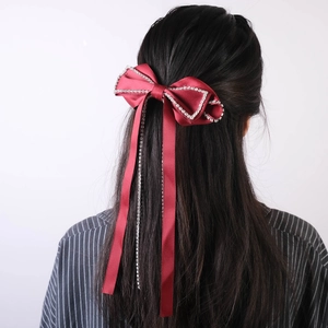 Close-up of burgundy satin bow hair clip with rhinestone edges and long tassels