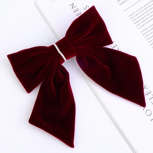 Close-up of a burgundy velvet bow hair clip with decorative pearls on a magazine