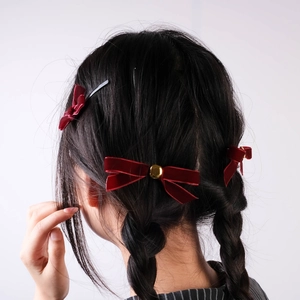Deep red velvet bow hair clips with gold center beads worn by a model in braids