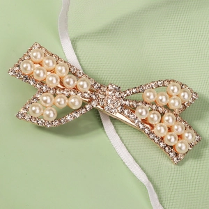 Détail de la pince à cheveux noeud avec strass brillants et perles sur base dorée