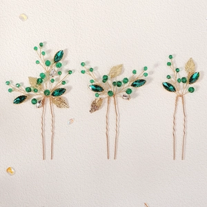 Detail view of handmade gold wire hair pins with green crystals and metal leaves