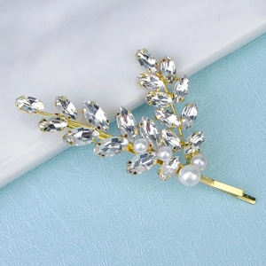 Detail of leaf-shaped hair clip with sparkling rhinestones and white pearls on gold metal