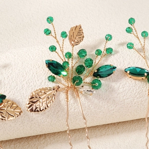 Detail of bridal hair pin with green crystals and gold leaves on a white background