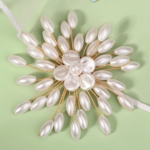 Macro detail of handmade floral brooch featuring white teardrop pearls and gold wire