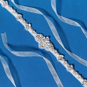Eleganter Brautgürtel mit funkelnden Strasssteinen und weißen Perlen auf blauem Stoff