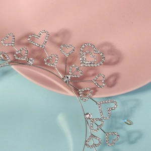 Vue détaillée du serre-tête cœur argenté avec cristaux sur plateau rose et fond bleu