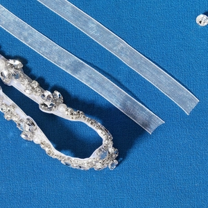 Detailansicht eines Brautgürtels mit Kristallen und Perlen auf weißem Satinband