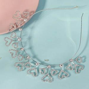 Détail d'un serre-tête argenté en forme de cœur avec strass sur fond bleu clair