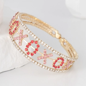 Bracelet jonc XOXO doré avec strass roses et rouges étincelants sur socle marbre