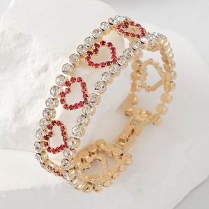 Detail van een gouden gelaagde armband met rode en witte strass hartvormige bedels op steen