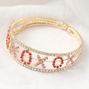 Gros plan d'un bracelet XOXO doré avec strass roses et rouges sur fond de soie blanche