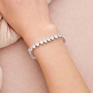 Gros plan d'un bracelet de tennis en zircons taille cœur porté sur fond de soie douce