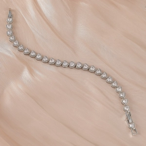 Gros plan d'un bracelet coeur en argent avec zircone sur un fond en soie champagne