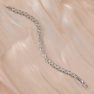 Détail d'un bracelet de tennis en argent en forme de cœur sur du satin champagne