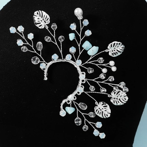 Gros plan détaillé sur un earcuff artisanal en fil d'argent avec cristaux et feuilles