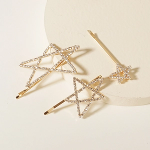 Close-up of three gold star hair clips with sparkling rhinestones on a stone display