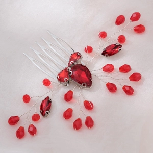 Detailed view of bridal hair comb with red crystals and silver wire on white silk fabric