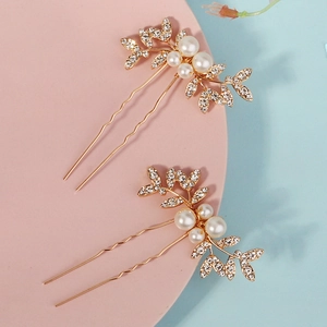Detail of two gold U-shaped bridal hair pins with inlaid rhinestones and white pearls