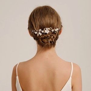 Dettaglio ravvicinato del pettine per capelli da sposa con foglie dorate e fiori bianchi