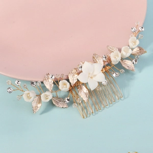 Dettaglio macro di fiori in ceramica bianca e foglie dorate su un pettine per capelli da sposa