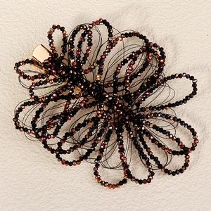 Handmade black beaded flower hair clip with golden alligator clasp on beige background