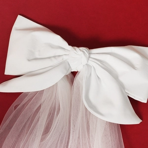 Detail of elegant white satin bow bridal veil with fine mesh texture on red background