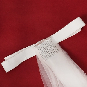 Close-up of white bridal veil with satin ribbon and metal hair comb on red background