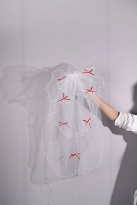 Detail of white double-layer bridal veil featuring red ribbon bows and pearl bead trim