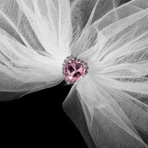 Detail of pink heart-shaped gemstone with rhinestone border on white bridal mesh veil