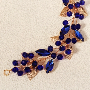 Dettaglio macro della fascia fatta a mano in filo d'oro con cristalli blu e foglie in metallo
