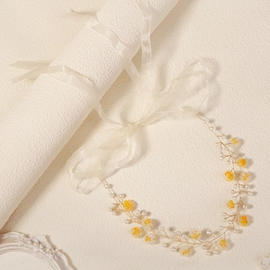 Close-up of yellow fabric flowers and white pearls on golden wire bridal headband