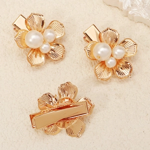 Vue détaillée de trois pinces à cheveux fleur dorée avec perles blanches sur fond texturé