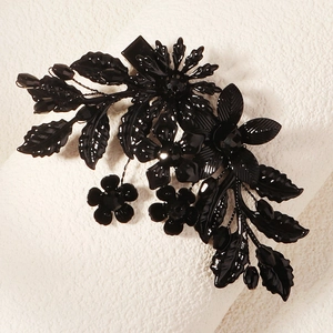 Détail d'une pince à cheveux fleurie noire aux pétales facettés et détails de feuilles