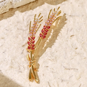 Macro shot of gold wheat brooch with gradient zircon crystals on beige textured paper